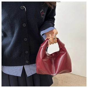 Détail du sac dumpling en cuir bordeaux avec poignée nouée et fermeture éclair sur modèle