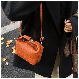 Détail du sac orange vif avec texture tissée, fermoir pivotant et bandoulière réglable