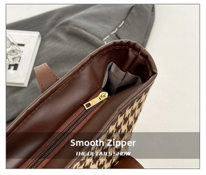 Detail of smooth gold metal zipper on houndstooth tote bag with brown leather trim
