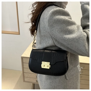 Detail of black crocodile texture bag with gold rectangular lock and metal chain strap