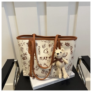 Detail view of cream tote bag with brown graffiti patterns and a cute bear charm