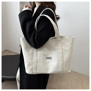 Detail view of large corduroy tote bag in off-white finish worn over a black coat