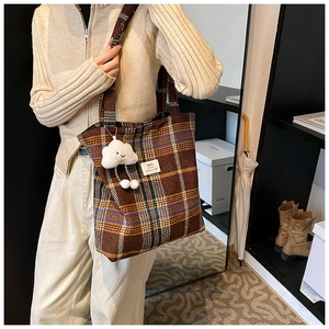 Detail of brown plaid tote bag featuring a plush white charm and brand woven label