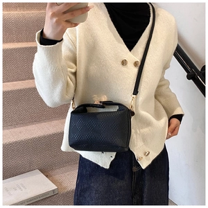 Détail d'un sac bandoulière tressé noir avec boucles dorées porté par un mannequin