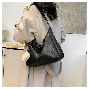 Detail of black PU leather shoulder bag with plush charm on a beige winter coat