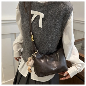 Detail of a brown leather crescent bag featuring golden hardware and plush ball charms