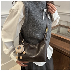 Détail d'un sac hobo en cuir marron foncé avec un charm mouton en peluche et texte blanc