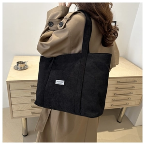 Detail of black corduroy tote bag showing the fashion label and ribbed fabric texture