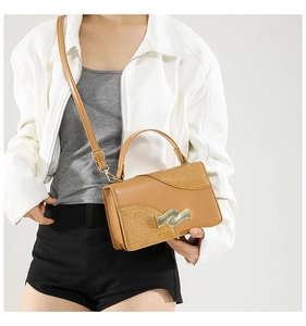 Detail of tan crossbody bag featuring crocodile texture and gold wavy buckle