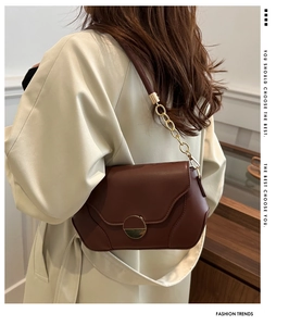 Detail of dark brown leather crossbody bag with round gold buckle and chain strap