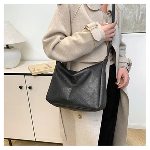 Detail of minimalist black PU leather crossbody bag worn with a beige autumn coat