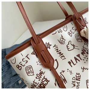 Detailed close-up of graffiti print tote bag with brown leather handles and heart charm