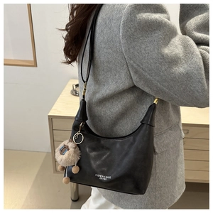 Detail of black leather hobo bag with white lettering and a cute plush lamb charm