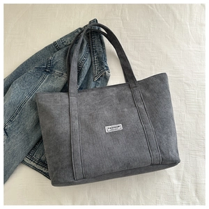 Macro shot of dark grey corduroy tote bag showing ribbed texture and fashion label