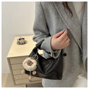 Détail d'un sac dumpling en cuir noir avec un charm en peluche marron et lettrage