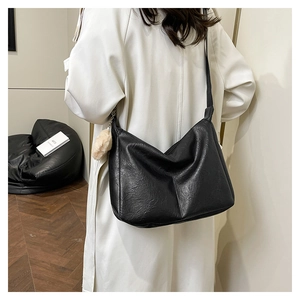 Detail of a large black leather hobo bag with a pompom charm worn over a white coat