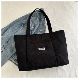 Detail of black corduroy tote bag featuring a white Fashion Instinct stitched label