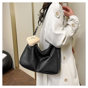Detail of black textured soft leather tote bag with plush smiley face charm on a white coat