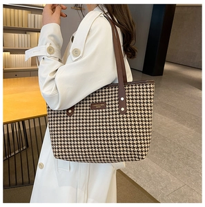 Detailed view of houndstooth tote bag with brown leather handle on a white coat model