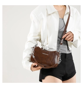 Detailed close-up of dark brown faux leather shoulder bag with gold chain and text engraving