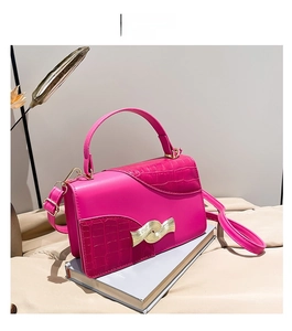 Détail du sac bandoulière rose fuchsia avec texture croco et boucle dorée ondulée