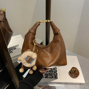 Sac à main marron avec pendentif mouton et bandoulière réglable tenu à la main