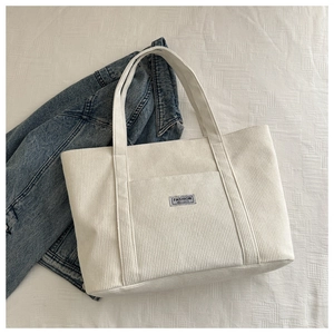 Detail of cream corduroy tote bag with fashion label and textured front pocket