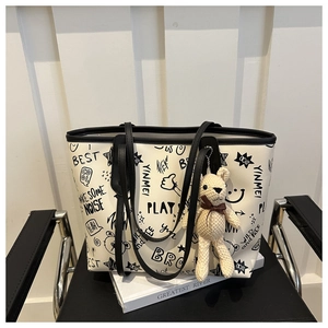 Detail of cream tote bag with black graffiti prints and a cute knitted bear charm