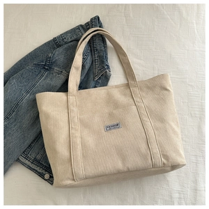 Detail of cream corduroy tote bag with textured stripes and fashion instinct patch