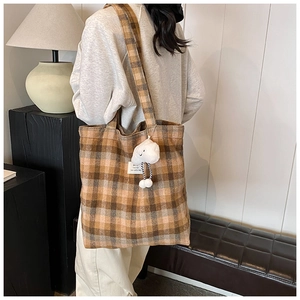 Detailed close-up of brown plaid tote bag with plush cloud charm and white woven label