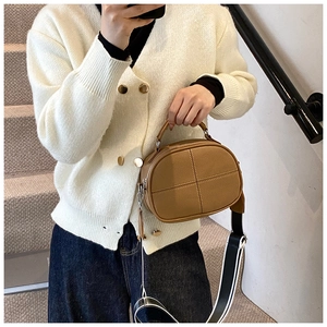 Detail of brown leather crossbody bag with cross stitching and striped fabric strap