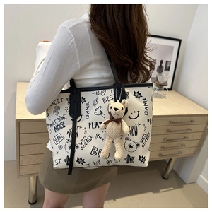 Detail of white tote bag with black graffiti prints and cute teddy bear charm