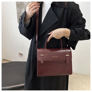 Détail d'un sac messager vintage bordeaux avec boucles dorées sur un manteau noir