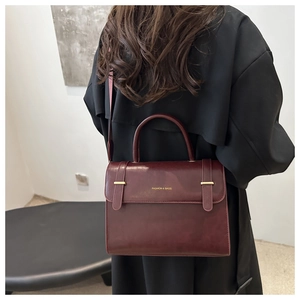 Detail of burgundy leather satchel with gold hardware against a black coat backdrop