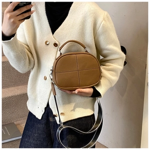 Close-up of brown textured leather crossbody bag featuring cross stitching and striped strap