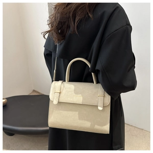 Detail of minimalist cream crossbody bag with gold buckles on a black coat model
