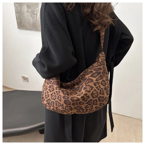 Detail of a large leopard print crescent tote bag worn over a black wool coat