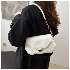 Détail d'un sac à rabat en cuir blanc avec chaîne dorée porté sur un manteau noir