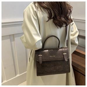 Detail of dark brown leather crossbody bag with gold buckle on a beige trench coat