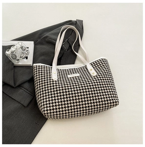 Close-up of large houndstooth tote bag featuring white leather straps and gold rivets