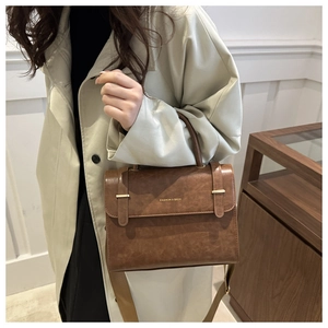Detail of a brown textured leather messenger bag with metal buckles and shoulder strap