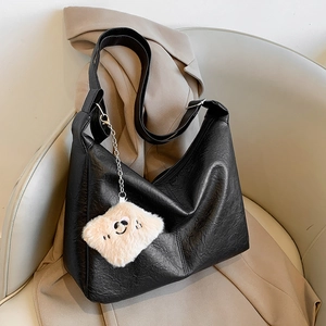 Large black minimalist leather tote bag with cute bear pendant on a chair