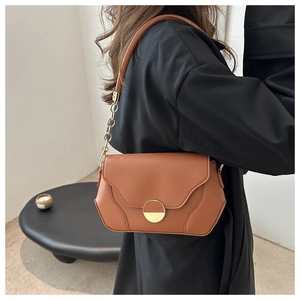 Sac à bandoulière en cuir marron avec boucle dorée porté par un mannequin femme