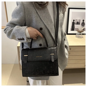 Détail d'un sac bandoulière noir avec boucle dorée sur un meuble minimaliste