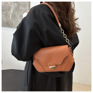 Brown leather crossbody bag detail featuring scalloped flap and gold round metal buckle