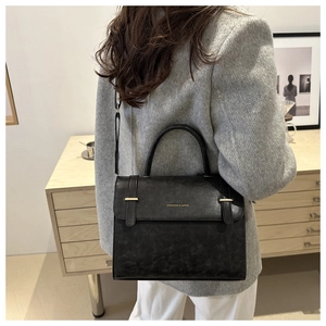 Detail of a chic black crossbody bag worn with a grey blazer in a stylish interior setting