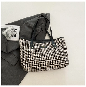 Detail of houndstooth tote bag featuring black leather trim and gold logo on gray blazer