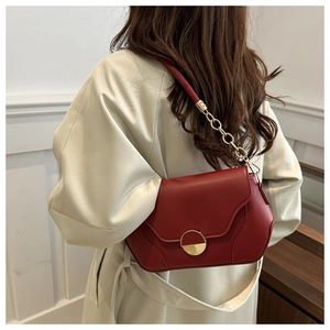Détail du sac bandoulière en cuir rouge avec fermoir doré sur un trench beige