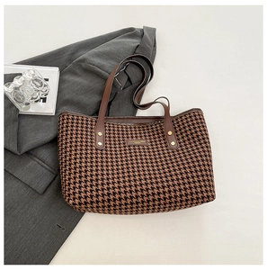 Detail of houndstooth tote bag with brown leather trim resting on a grey blazer