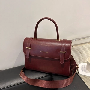 Burgundy PU leather messenger bag with wide shoulder strap and gold hardware on black surface